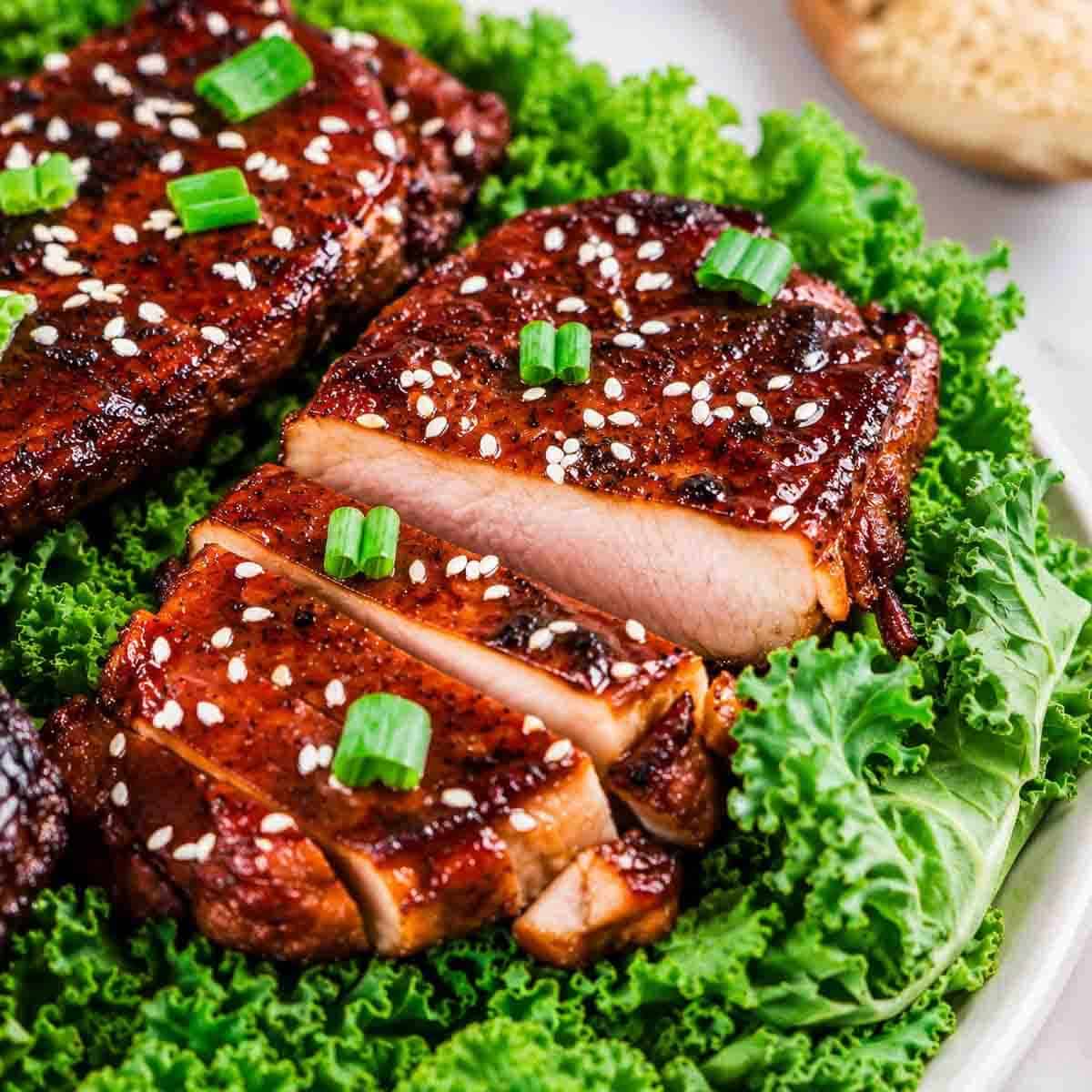 Sliced grilled pork chops glazed with a honey garlic soy sauce, topped with sesame seeds and chopped green onions, served on a bed of fresh green kale.