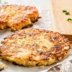 Two golden-brown crispy cauliflower hash brown patties resting on parchment paper.