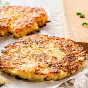 Two golden-brown crispy cauliflower hash brown patties resting on parchment paper.