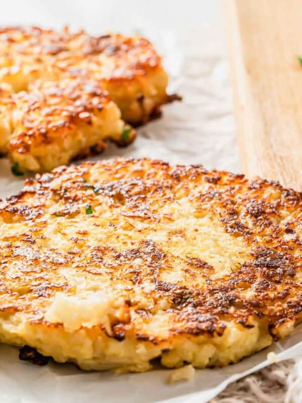 Two golden-brown crispy cauliflower hash brown patties resting on parchment paper.