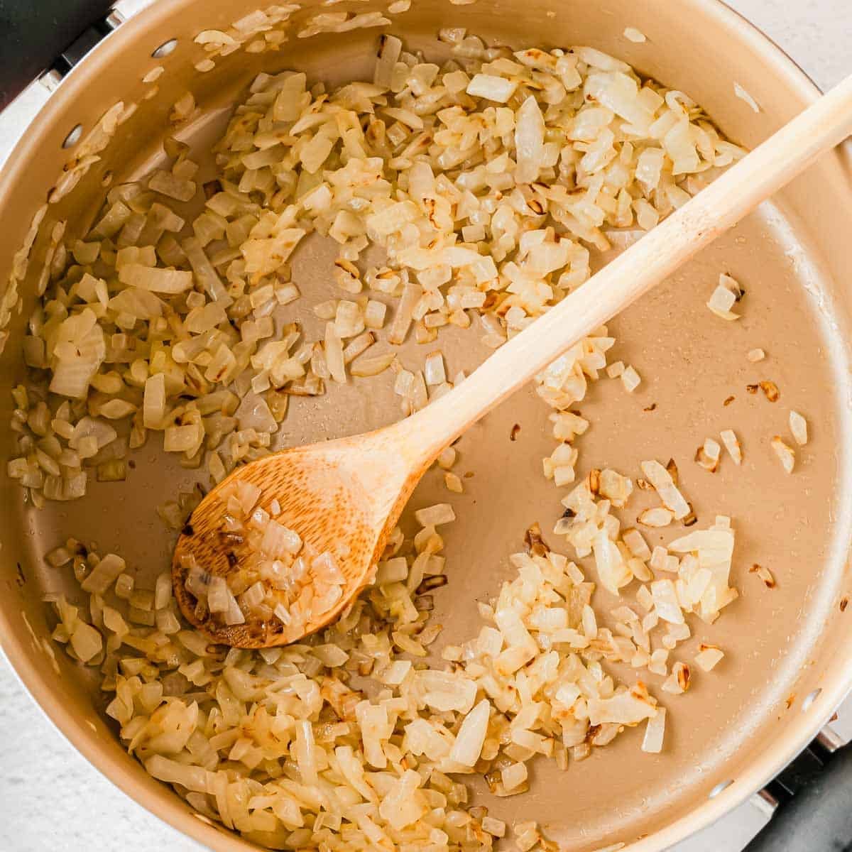 Diced onions saut&eacute;ing in a pan with a wooden spoon.