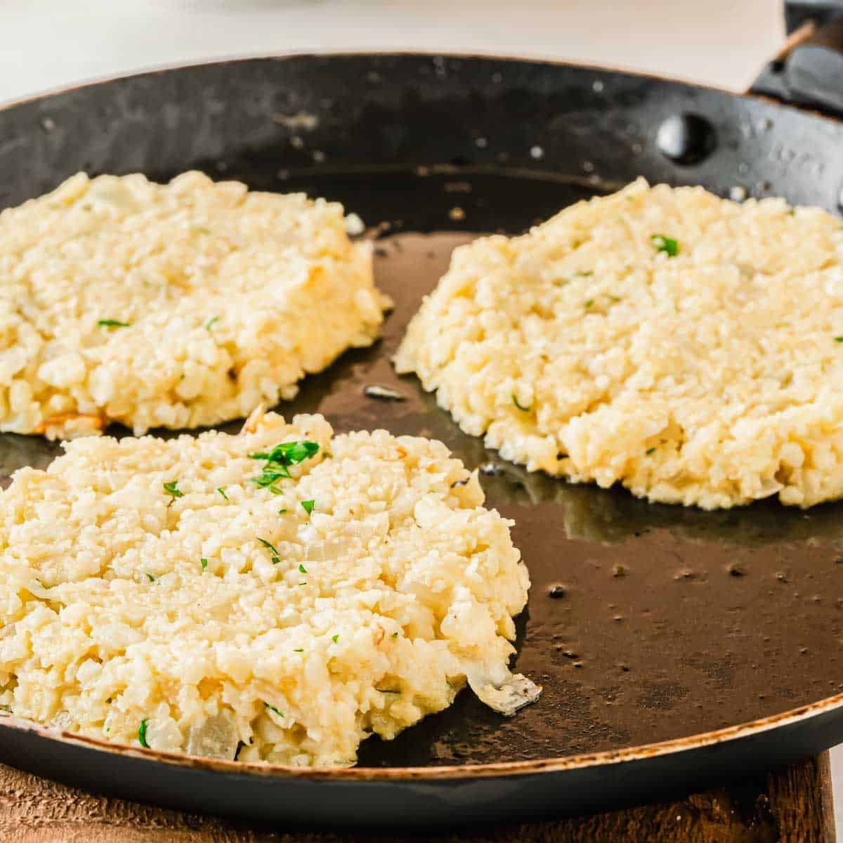 Three cauliflower hash browns frying in a pan.