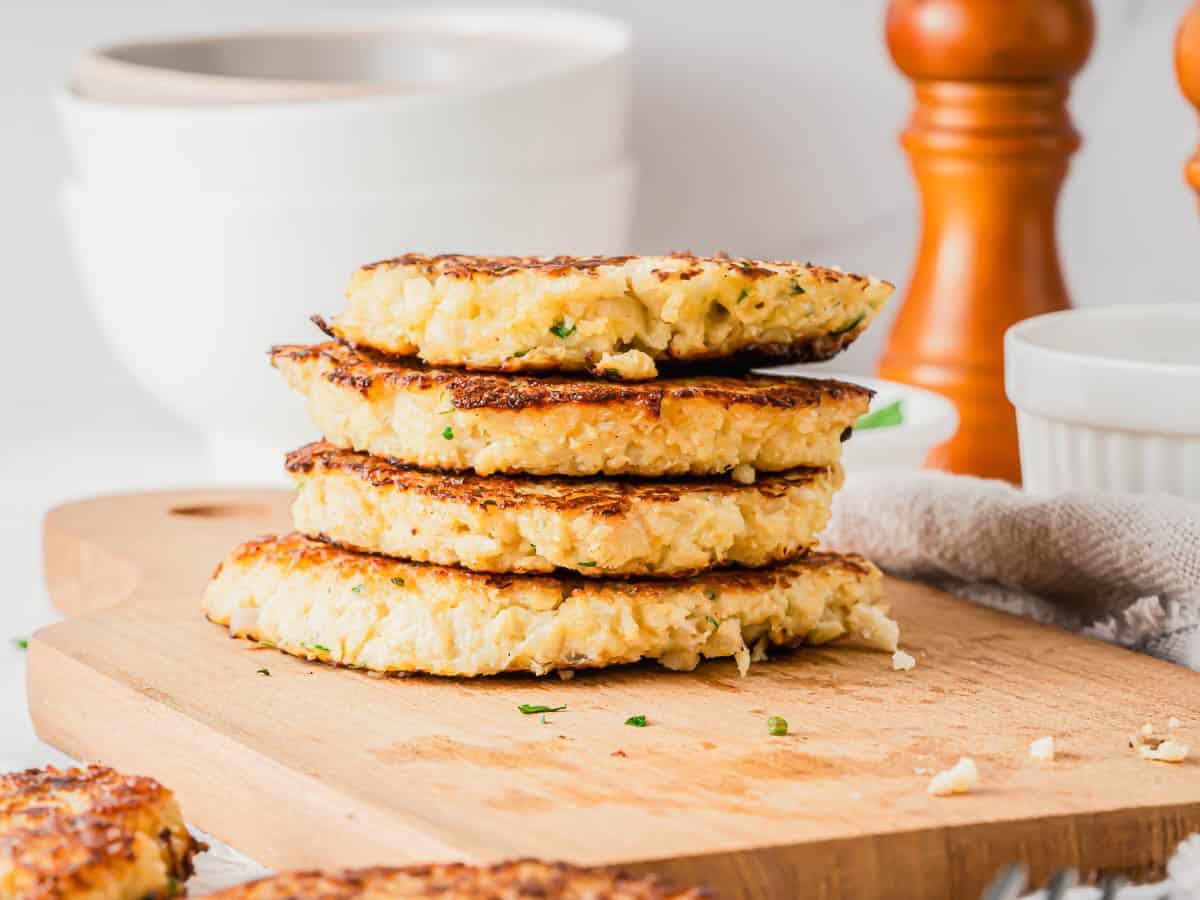 A stack of four golden-brown cauliflower fritters on a wooden cutting board.