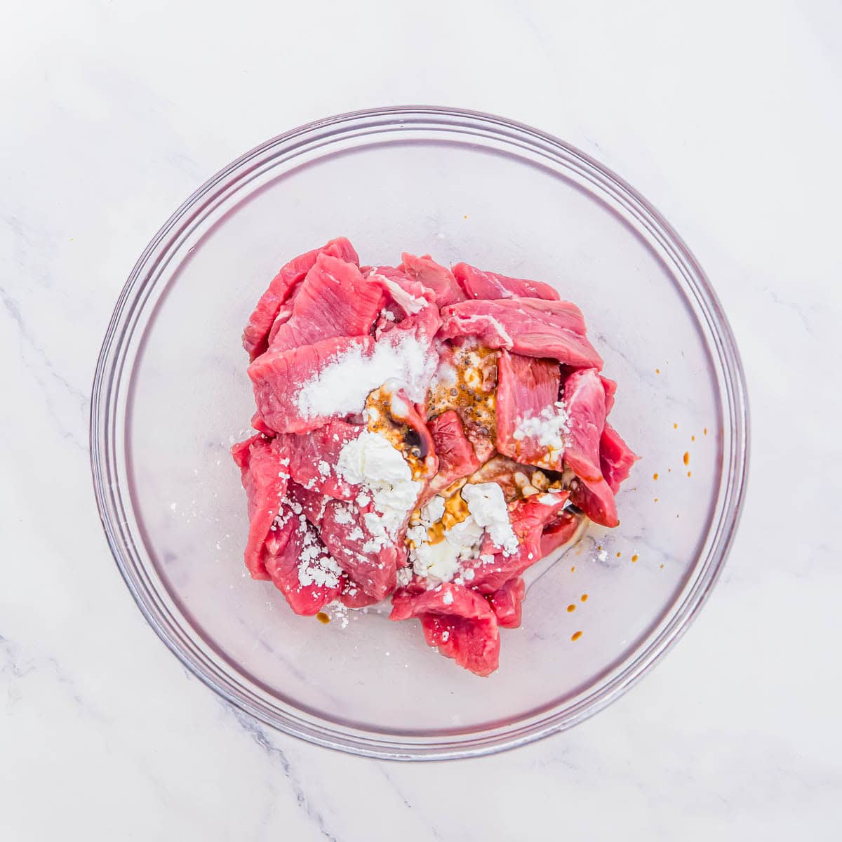 Raw beef strips in a glass bowl, coated with cornstarch and soy sauce marinade.