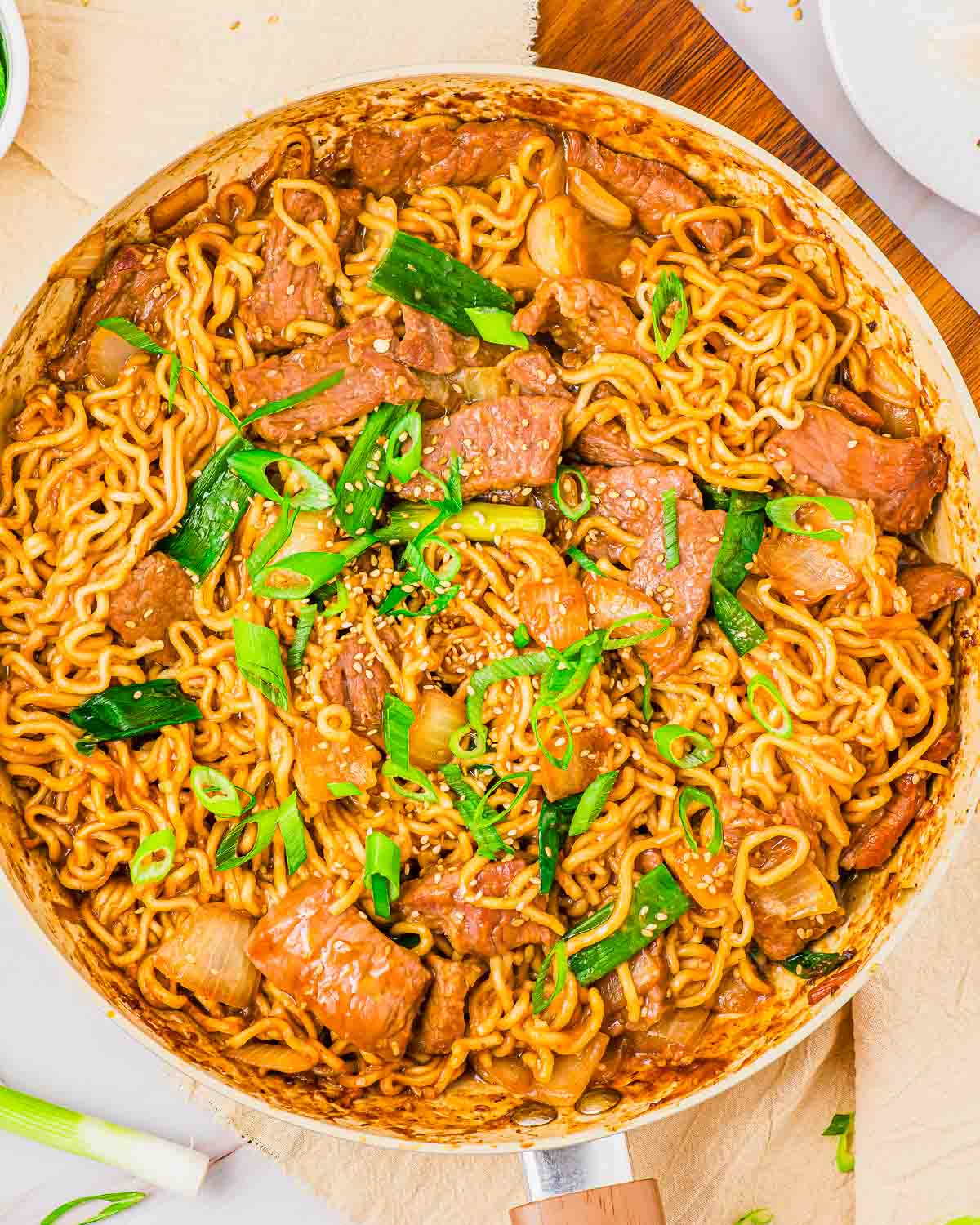 A pan of Mongolian beef stir-fry noodles garnished with green onions and sesame seeds.