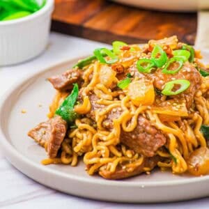 A plate of stir-fried ramen noodles with beef, vegetables, and sesame seeds.