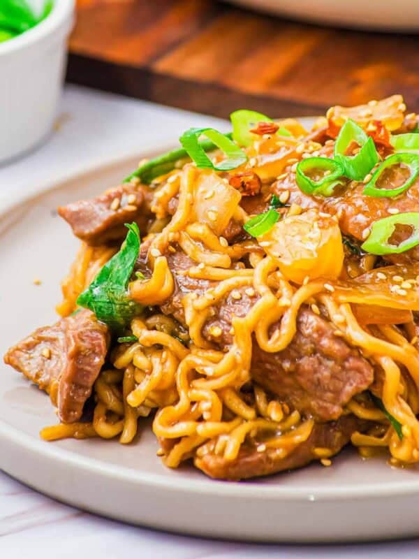 A plate of stir-fried ramen noodles with beef, vegetables, and sesame seeds.