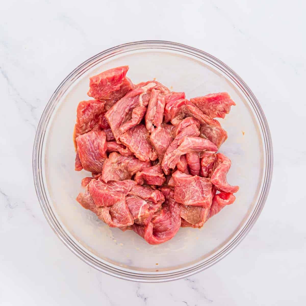 Strips of raw, marinated beef in a glass bowl.