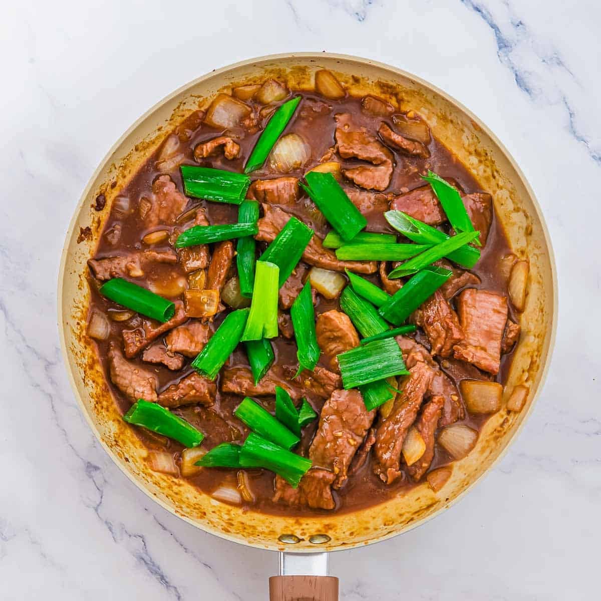 Beef and onion stir-fry in a brown sauce, topped with chopped green onions in a skillet.